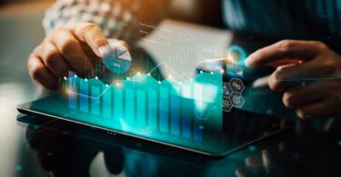 Pessoa utilizando tablet com gráficos digitais, dados e indicadores financeiros representando tecnologia e inteligência artificial no marketing imobiliário.