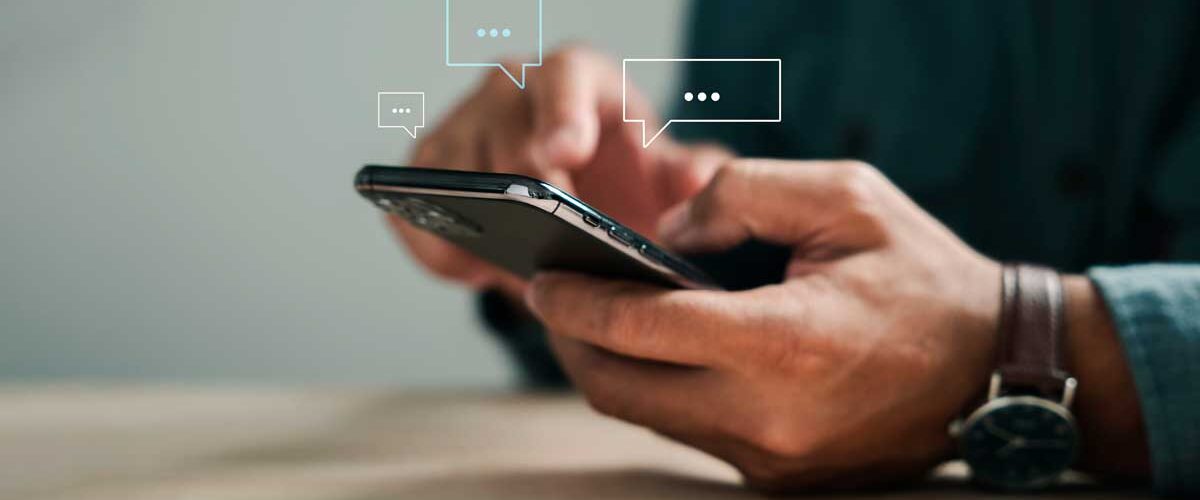 Pessoa manuseando smartphone com balões de conversa digitais, representando atendimento e suporte ao cliente via chatbot com inteligência artificial no mercado imobiliário.