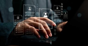 Mãos digitando em notebook com documentos digitais e checklists flutuando, representando o uso de inteligência artificial para captação, triagem e automação de leads no mercado imobiliário.