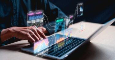 Pessoa usando notebook com gráficos digitais de análise de dados flutuando sobre a tela, simbolizando o uso de inteligência artificial e tecnologia avançada para interpretar informações e tendências no mercado imobiliário.